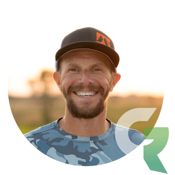 Smiling man with a beard wearing a baseball cap and a camouflage shirt.