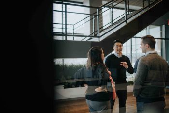 Three colleagues talking in a modern office space with a staircase in the background.