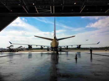 A passenger airplane seen from behind, parked outside an aircraft hangar.