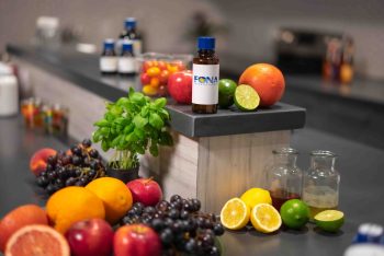 A bottle of FONA International flavoring surrounded by fresh fruit, herbs, and small glass jars.