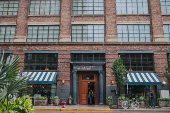Exterior of the brick Allis Building with blue-and-white striped awnings and a recessed wooden entrance.