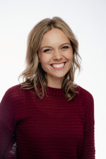 A woman smiling, wearing a maroon sweater against a white background.